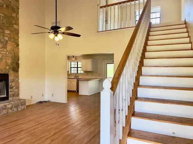 staircase with a fireplace, a high ceiling, ceiling fan, and wood-type flooring