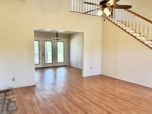 unfurnished living room featuring ceiling fan with notable chandelier, a high ceiling, and light wood-type flooring