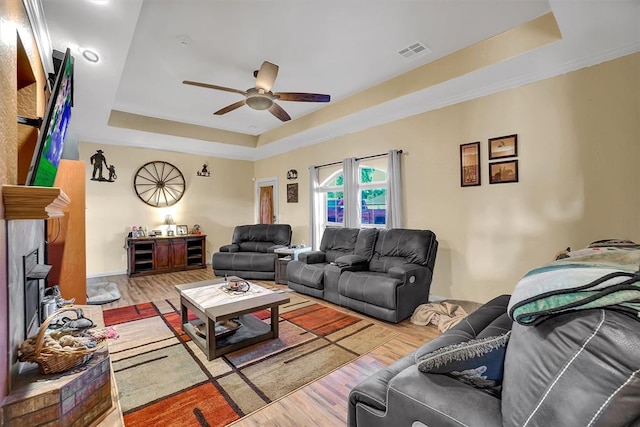 living room with ceiling fan, light hardwood / wood-style flooring, and a tray ceiling