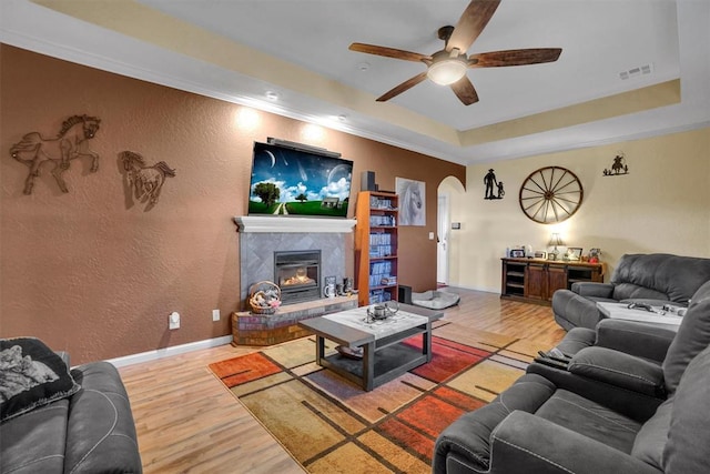 living room featuring hardwood / wood-style flooring, a raised ceiling, ceiling fan, and ornamental molding