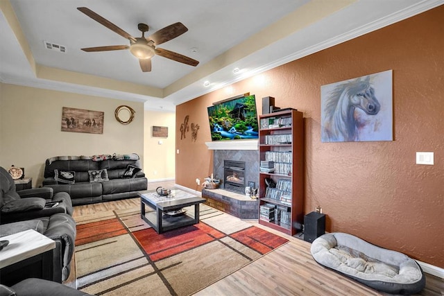 living room with hardwood / wood-style flooring, ceiling fan, ornamental molding, and a tray ceiling