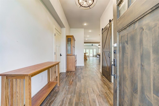 hall featuring a barn door, dark hardwood / wood-style floors, and a notable chandelier