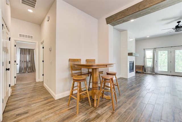 dining area with beam ceiling, ceiling fan, a fireplace, and hardwood / wood-style flooring