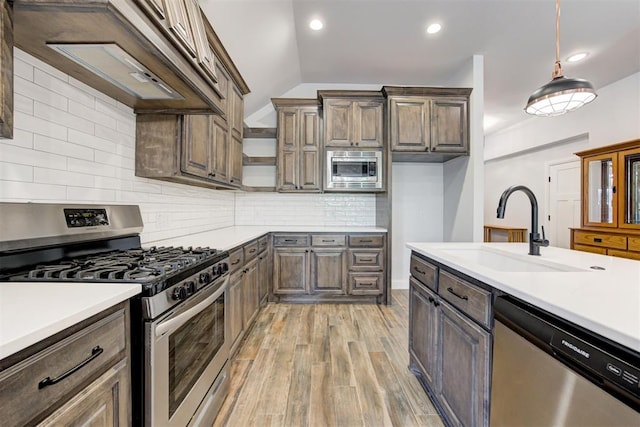 kitchen featuring sink, light hardwood / wood-style floors, decorative light fixtures, decorative backsplash, and appliances with stainless steel finishes