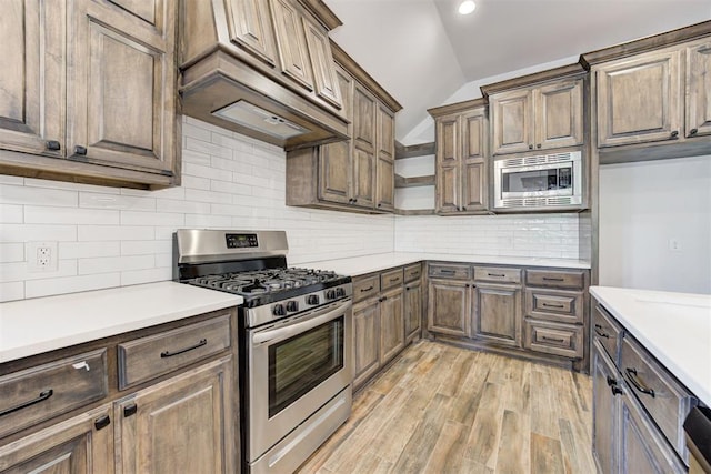 kitchen featuring decorative backsplash, light hardwood / wood-style flooring, vaulted ceiling, and appliances with stainless steel finishes