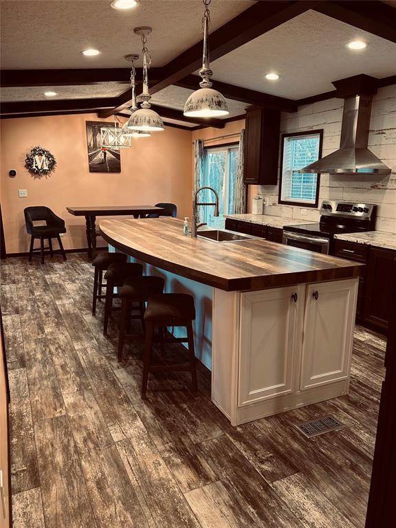 kitchen with dark brown cabinetry, sink, wall chimney range hood, butcher block counters, and stainless steel range with electric cooktop