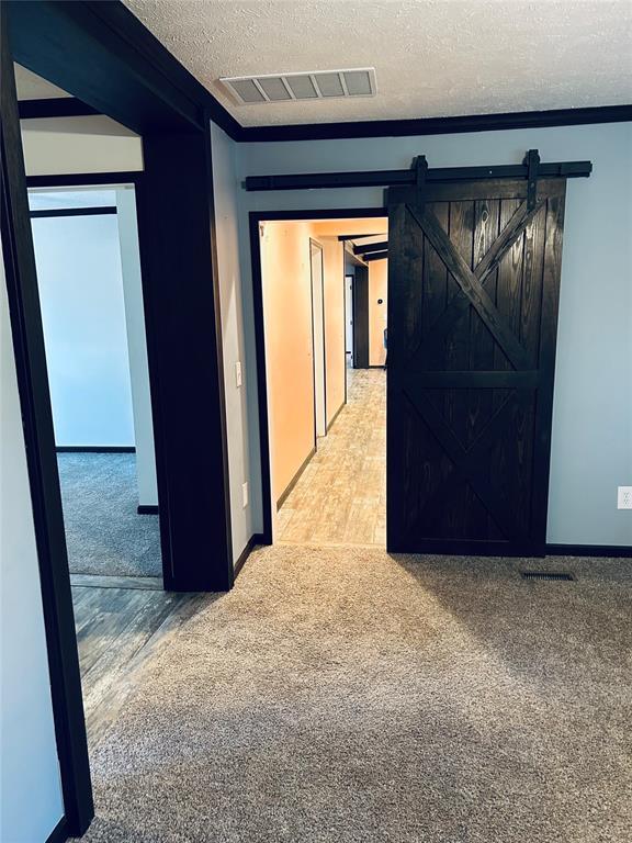 hallway with carpet flooring, a barn door, a textured ceiling, and ornamental molding