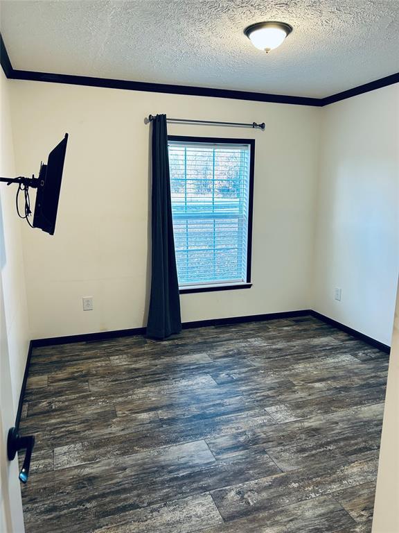 empty room featuring a textured ceiling, dark hardwood / wood-style floors, and crown molding