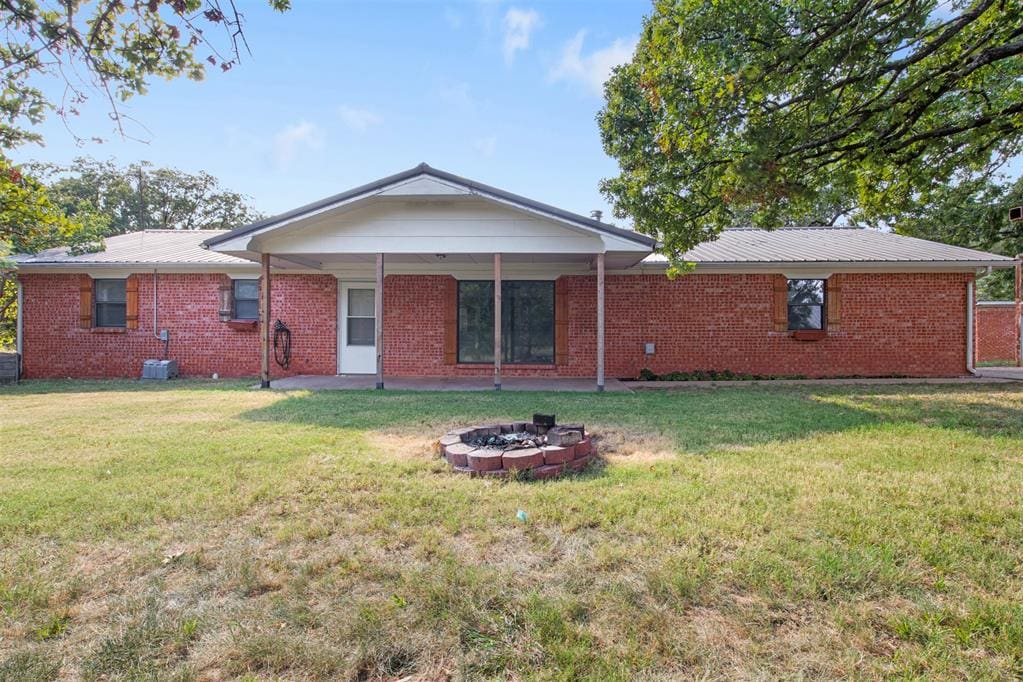 back of property with a yard and an outdoor fire pit