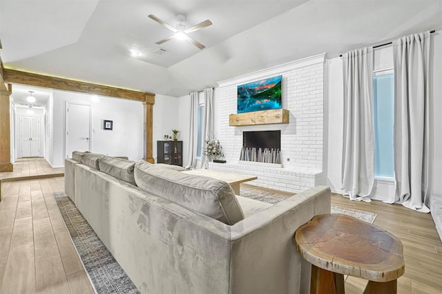 living room featuring a brick fireplace, ceiling fan, lofted ceiling, and light hardwood / wood-style flooring