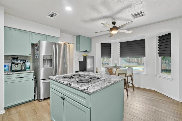 kitchen featuring ceiling fan, a center island, green cabinetry, light hardwood / wood-style floors, and appliances with stainless steel finishes