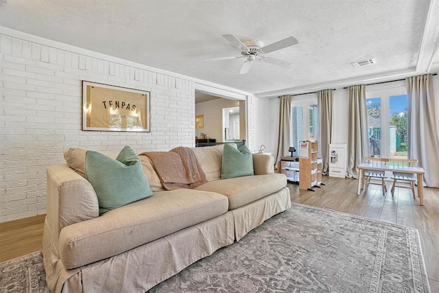 living room featuring ceiling fan, brick wall, a textured ceiling, and light wood-type flooring