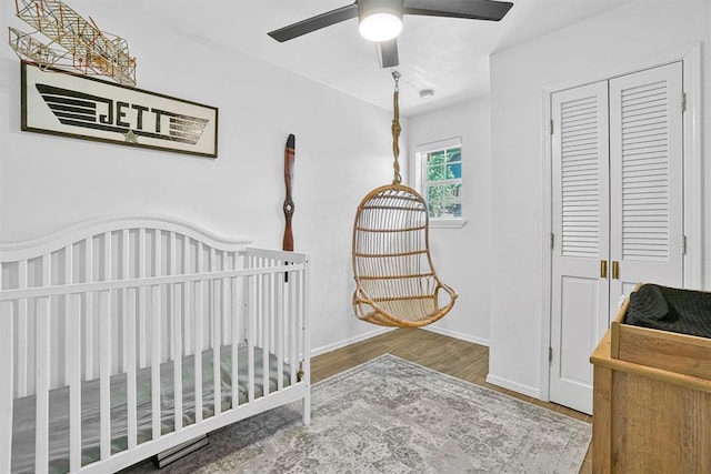 bedroom featuring ceiling fan, a closet, wood-type flooring, and a crib