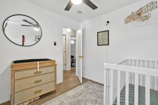 bedroom with hardwood / wood-style flooring, a nursery area, and ceiling fan