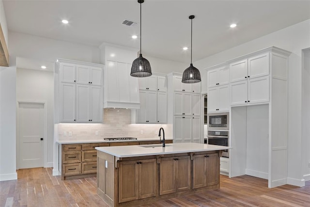 kitchen with sink, stainless steel appliances, an island with sink, light hardwood / wood-style floors, and white cabinets