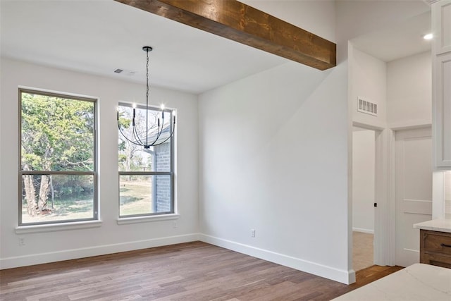 unfurnished dining area with beam ceiling, an inviting chandelier, and light wood-type flooring