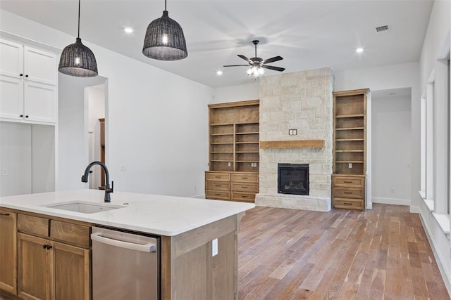 kitchen featuring white cabinets, a center island with sink, a stone fireplace, sink, and light hardwood / wood-style flooring