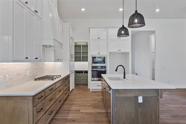 kitchen with pendant lighting, white cabinets, an island with sink, appliances with stainless steel finishes, and light hardwood / wood-style floors