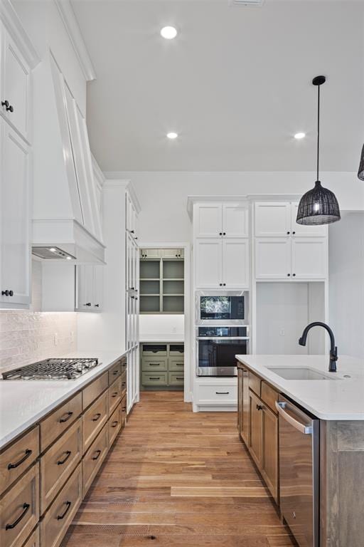 kitchen featuring premium range hood, stainless steel appliances, pendant lighting, white cabinets, and light hardwood / wood-style floors