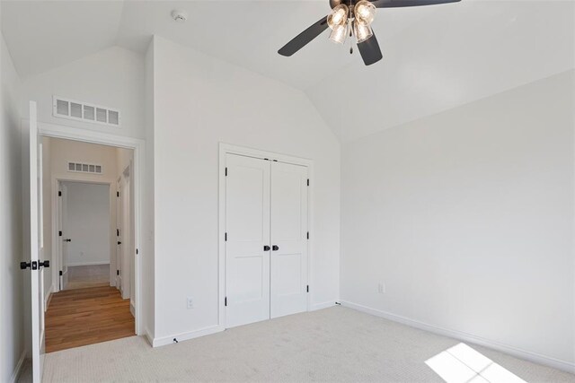 unfurnished bedroom with ceiling fan, a closet, light colored carpet, and vaulted ceiling