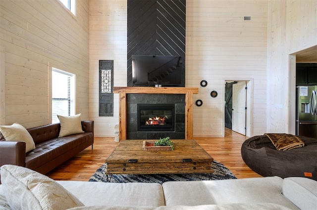 living room featuring wood walls, a towering ceiling, a tile fireplace, and light hardwood / wood-style flooring