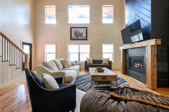 living room featuring a tile fireplace, wooden walls, a high ceiling, and light wood-type flooring