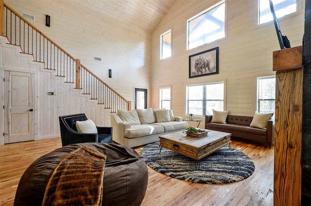 living room with wooden walls, high vaulted ceiling, and light hardwood / wood-style floors