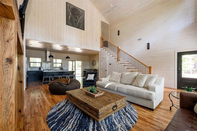 living room featuring wooden walls, light wood-type flooring, and high vaulted ceiling