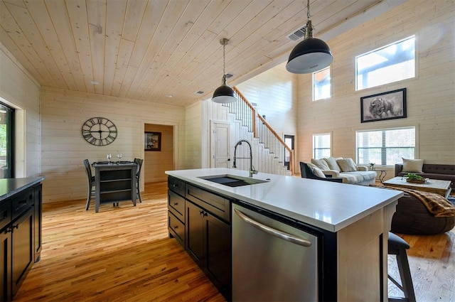 kitchen featuring stainless steel dishwasher, sink, pendant lighting, a center island with sink, and light hardwood / wood-style flooring