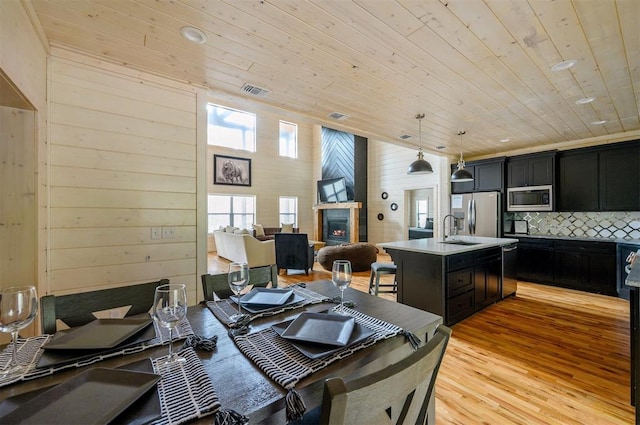 dining space with sink, light hardwood / wood-style flooring, wooden walls, and wood ceiling