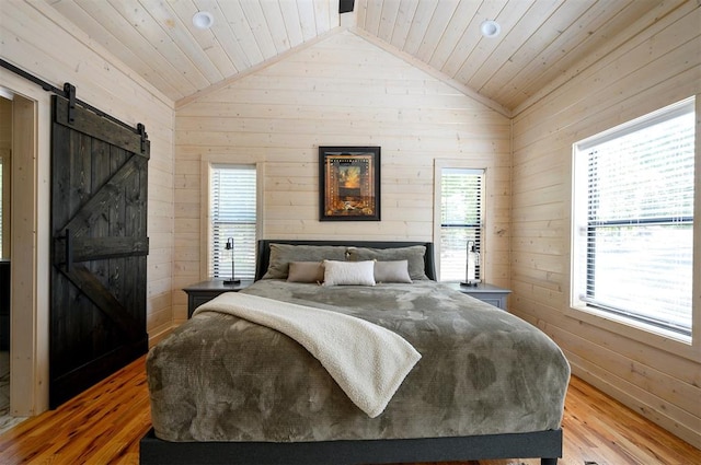 bedroom with a barn door, light hardwood / wood-style floors, multiple windows, and wooden walls