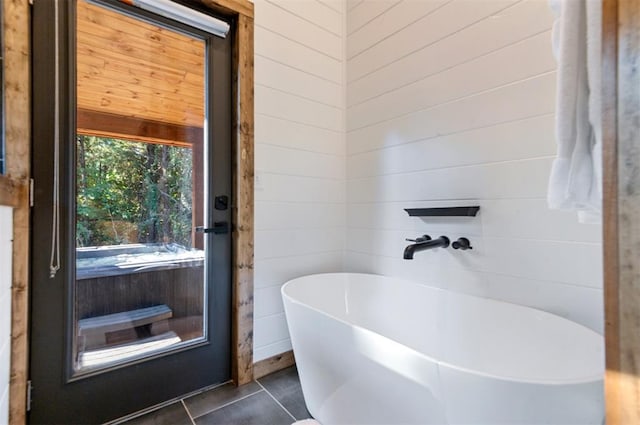 bathroom featuring a tub to relax in, tile patterned floors, and wooden walls