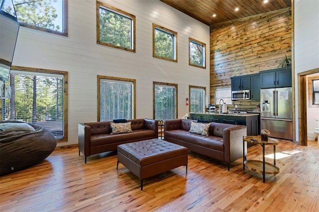 living room with wood walls, light wood-type flooring, wood ceiling, and high vaulted ceiling