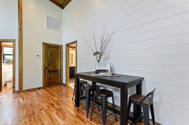 dining space with wood walls, wooden ceiling, high vaulted ceiling, and light hardwood / wood-style flooring