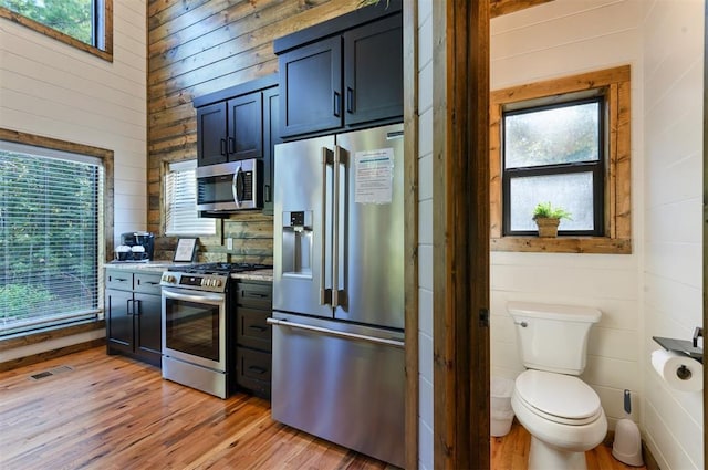 kitchen with wood walls, light hardwood / wood-style floors, light stone counters, and stainless steel appliances