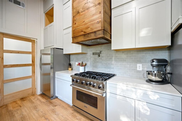 kitchen featuring decorative backsplash, appliances with stainless steel finishes, premium range hood, light hardwood / wood-style flooring, and white cabinets