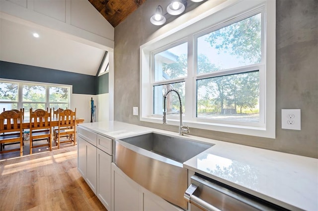 kitchen with stainless steel dishwasher, vaulted ceiling, sink, light hardwood / wood-style floors, and white cabinetry