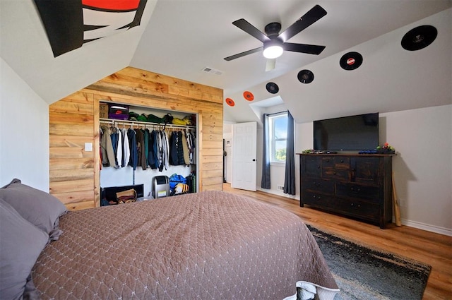 bedroom featuring hardwood / wood-style floors, wood walls, lofted ceiling, ceiling fan, and a closet