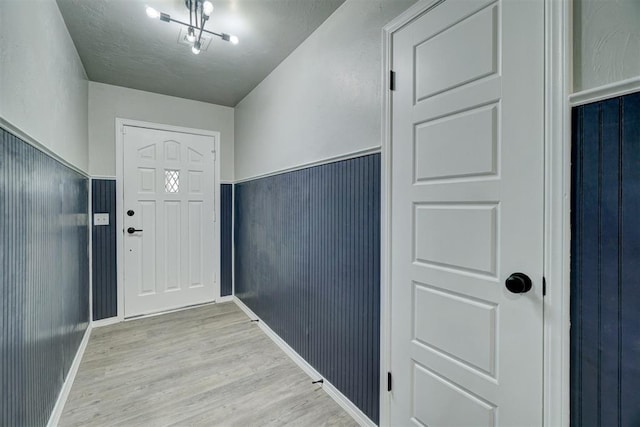 entrance foyer with light wood-type flooring, a textured ceiling, wooden walls, and a chandelier