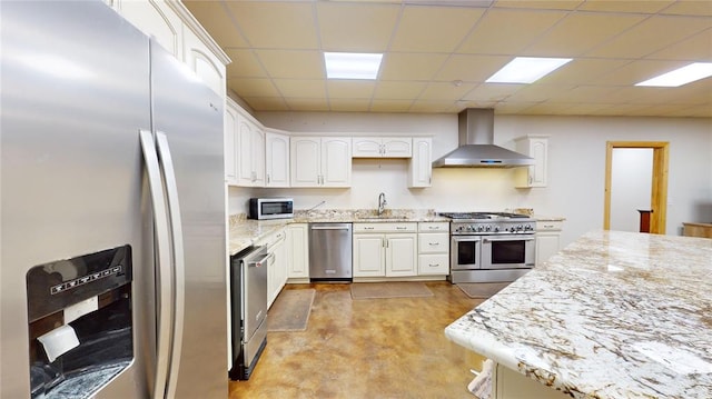 kitchen with appliances with stainless steel finishes, a paneled ceiling, wall chimney exhaust hood, sink, and white cabinets