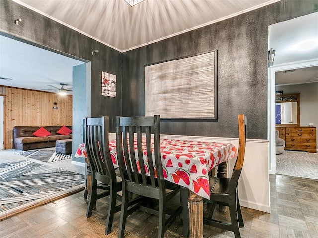 dining room with wooden walls, ceiling fan, and ornamental molding