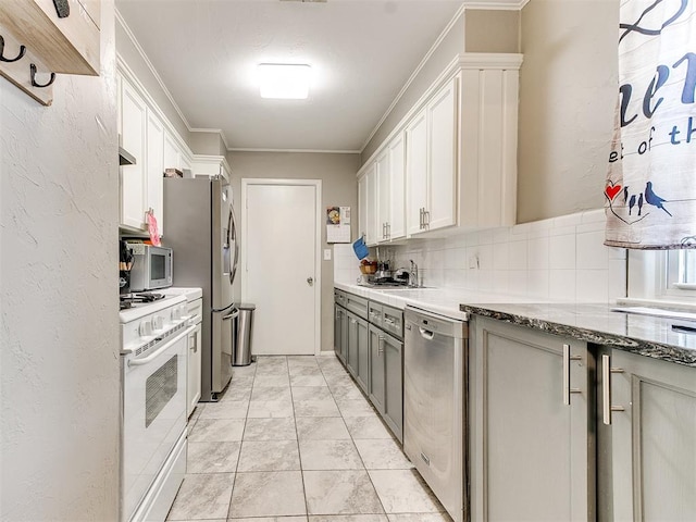 kitchen with decorative backsplash, appliances with stainless steel finishes, ornamental molding, dark stone counters, and white cabinetry