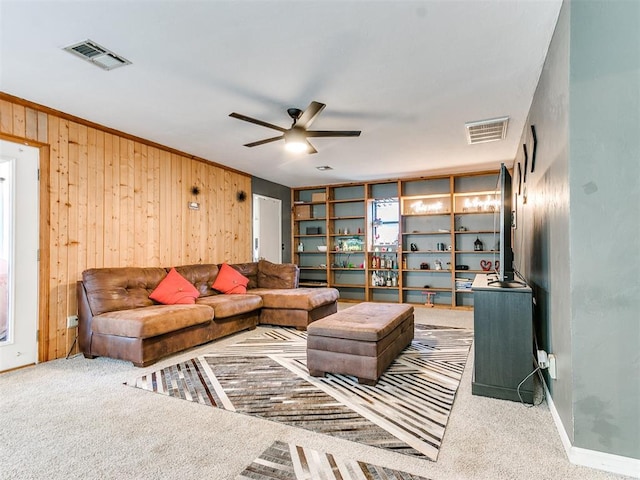 living room with ceiling fan, wooden walls, carpet, and ornamental molding