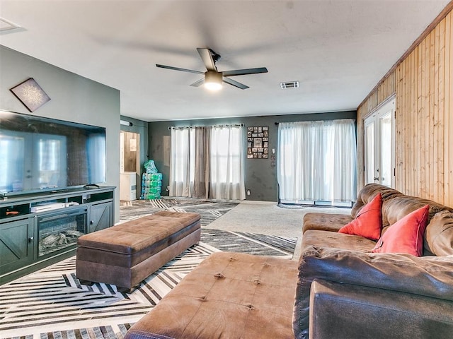 carpeted living room with wooden walls, a fireplace, and ceiling fan