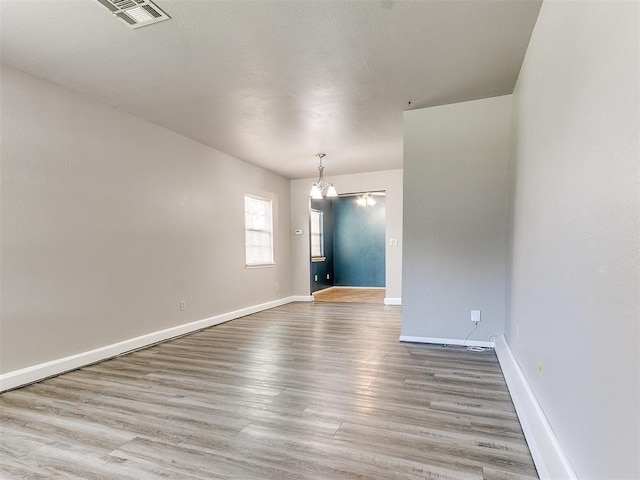 spare room featuring light wood-type flooring and an inviting chandelier