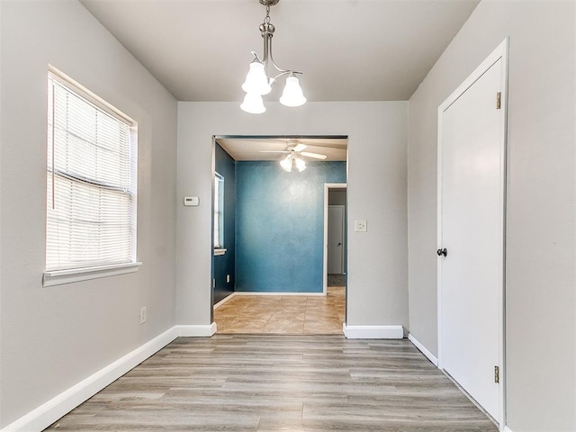 unfurnished dining area featuring ceiling fan with notable chandelier and light hardwood / wood-style flooring