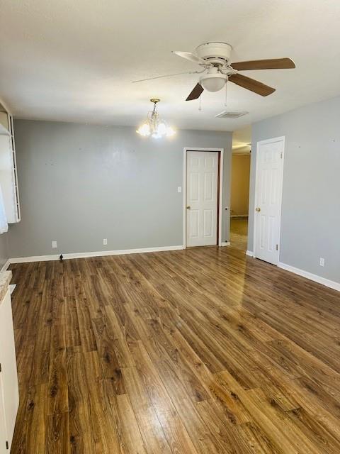 empty room featuring ceiling fan with notable chandelier and dark hardwood / wood-style floors