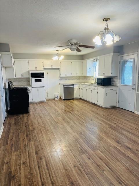 kitchen featuring white oven, white cabinetry, stainless steel dishwasher, decorative light fixtures, and ceiling fan with notable chandelier