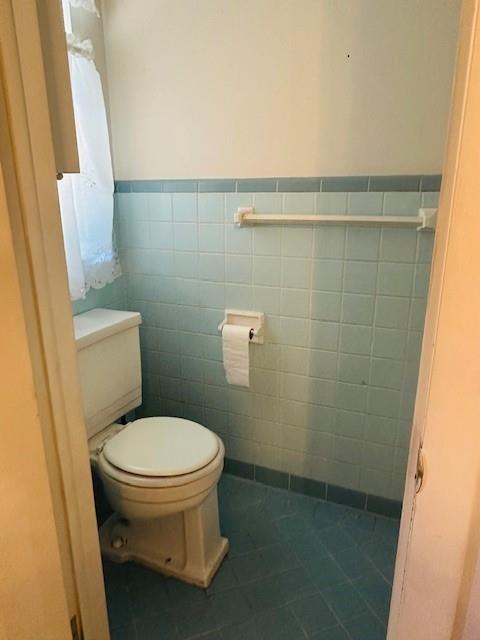 bathroom with toilet, tile patterned flooring, and tile walls