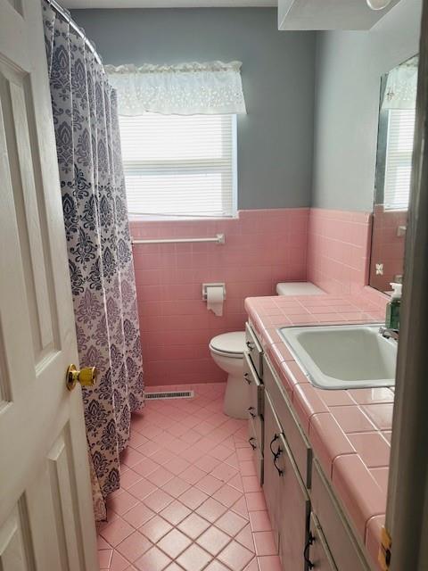 bathroom with tile patterned flooring, vanity, tile walls, toilet, and walk in shower